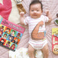 Baby wearing a 'Girl Power' onesie with books on a pink blanket