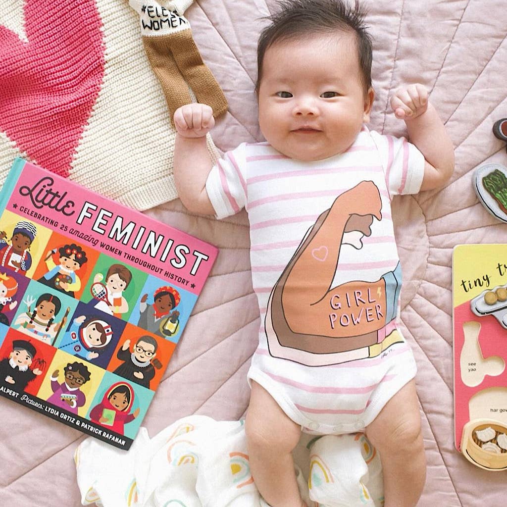Baby wearing a 'Girl Power' onesie with books on a pink blanket