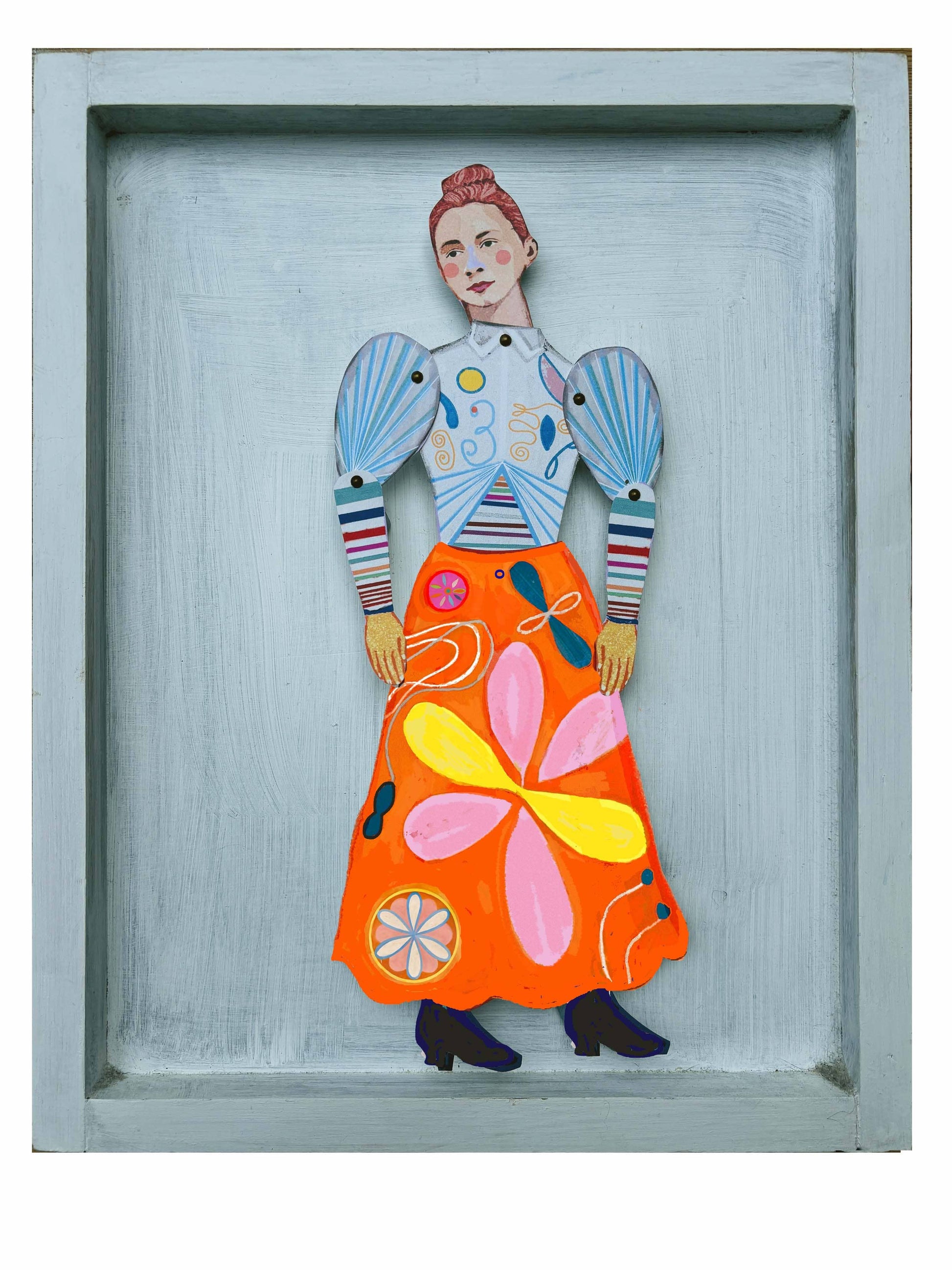 Colorful paper sculpture of a woman with a floral skirt in a gray frame