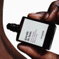Hand holding a bottle of Versace Gueule de Bois perfume against a white background