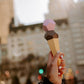 Hand holding a geometric ice cream cone toy with a cityscape in the background