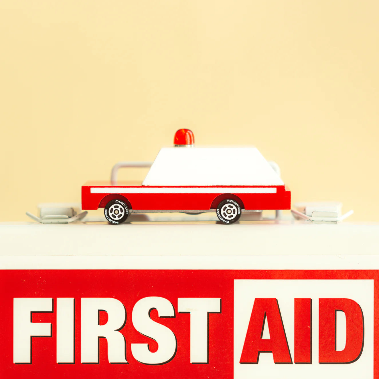 Red and white toy ambulance on a beige background with 'FIRST AID' text.