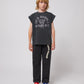 A young model wears the trousers with a black sleeveless graphic t-shirt featuring the text "Joy is opening a letter with my name on it." The trousers have a relaxed fit and are paired with multicoloured sporty sandals.