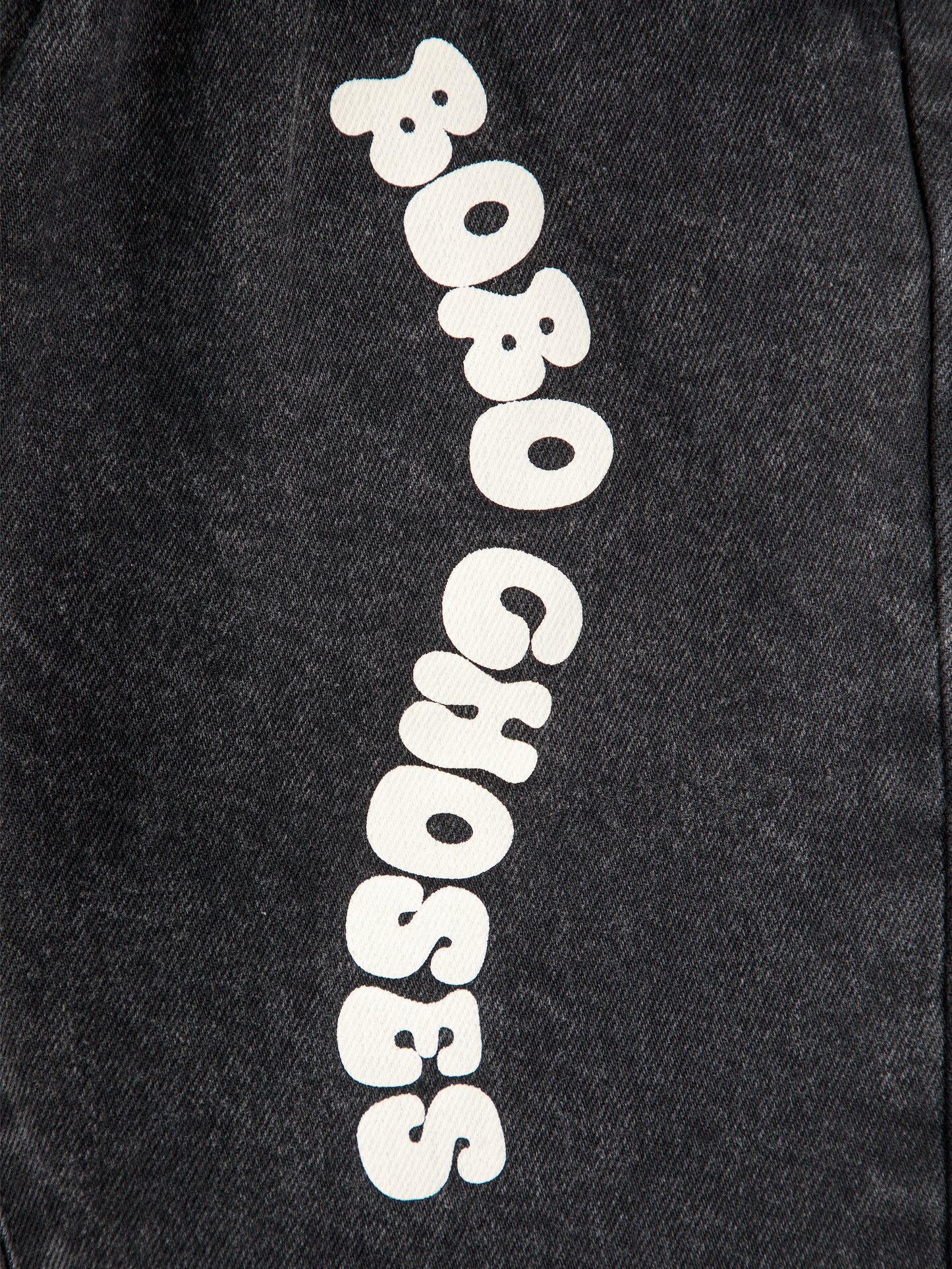 A detailed view of the white "Bobo Choses" lettering on the left leg, contrasting against the black denim fabric.