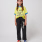 A young model wears the trousers paired with a yellow graphic t-shirt, colourful sneakers, and a red-and-white cap. The relaxed fit and casual style of the trousers are showcased.