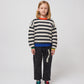 Another child models the trousers with a black-and-white striped knitted jumper, blue-and-black trainers, and the trousers slightly cuffed at the hem.