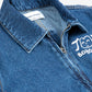 A close-up of the collar and upper chest area of a dark blue denim jumpsuit. The structured collar has visible stitching, and a partially unzipped metal zipper runs down the front. A white "JOY BOBO CHOSES" logo with a smiling face is printed on the left chest. Inside the collar, a white label displays the brand name "BOBO CHOSES" and size details. The fabric has a slightly worn texture.