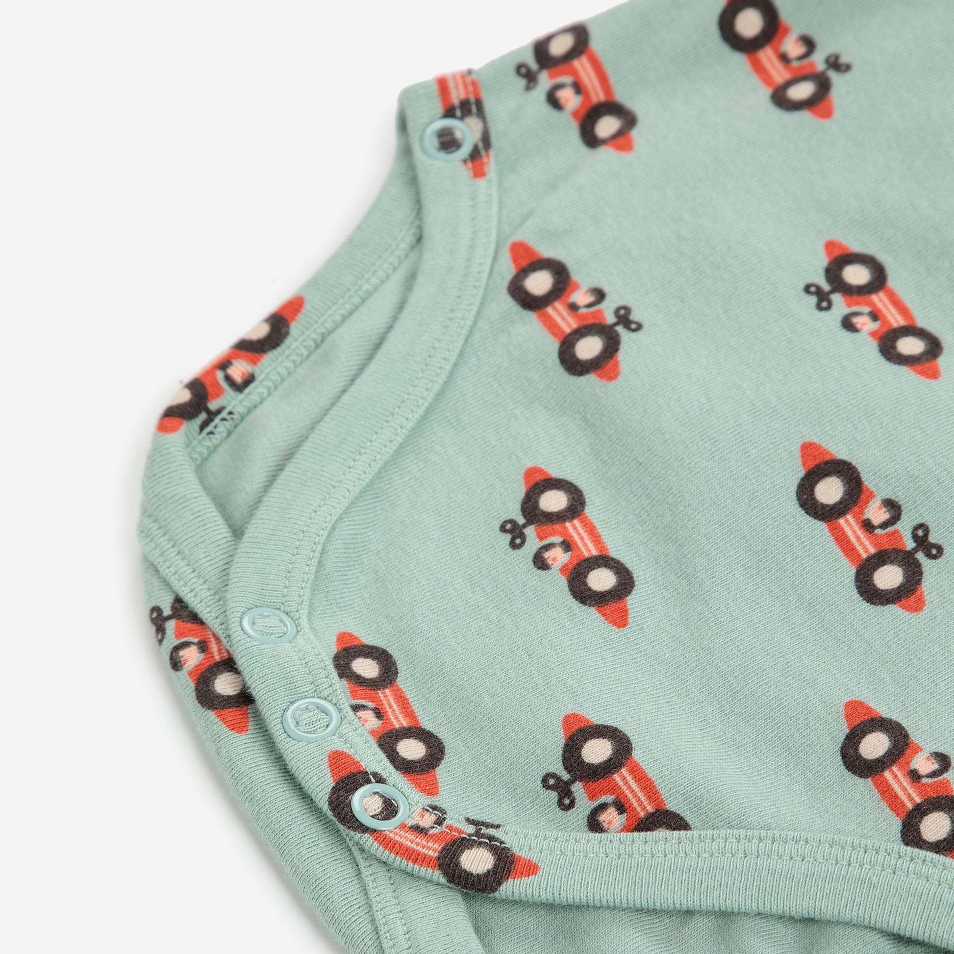 Green baby onesie with red tractor pattern on a white background