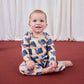 Baby sitting on a red floor wearing a patterned outfit with a white curtain background