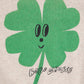 Green four-leaf clover with a face and 'Bobo Choses' text on a beige background