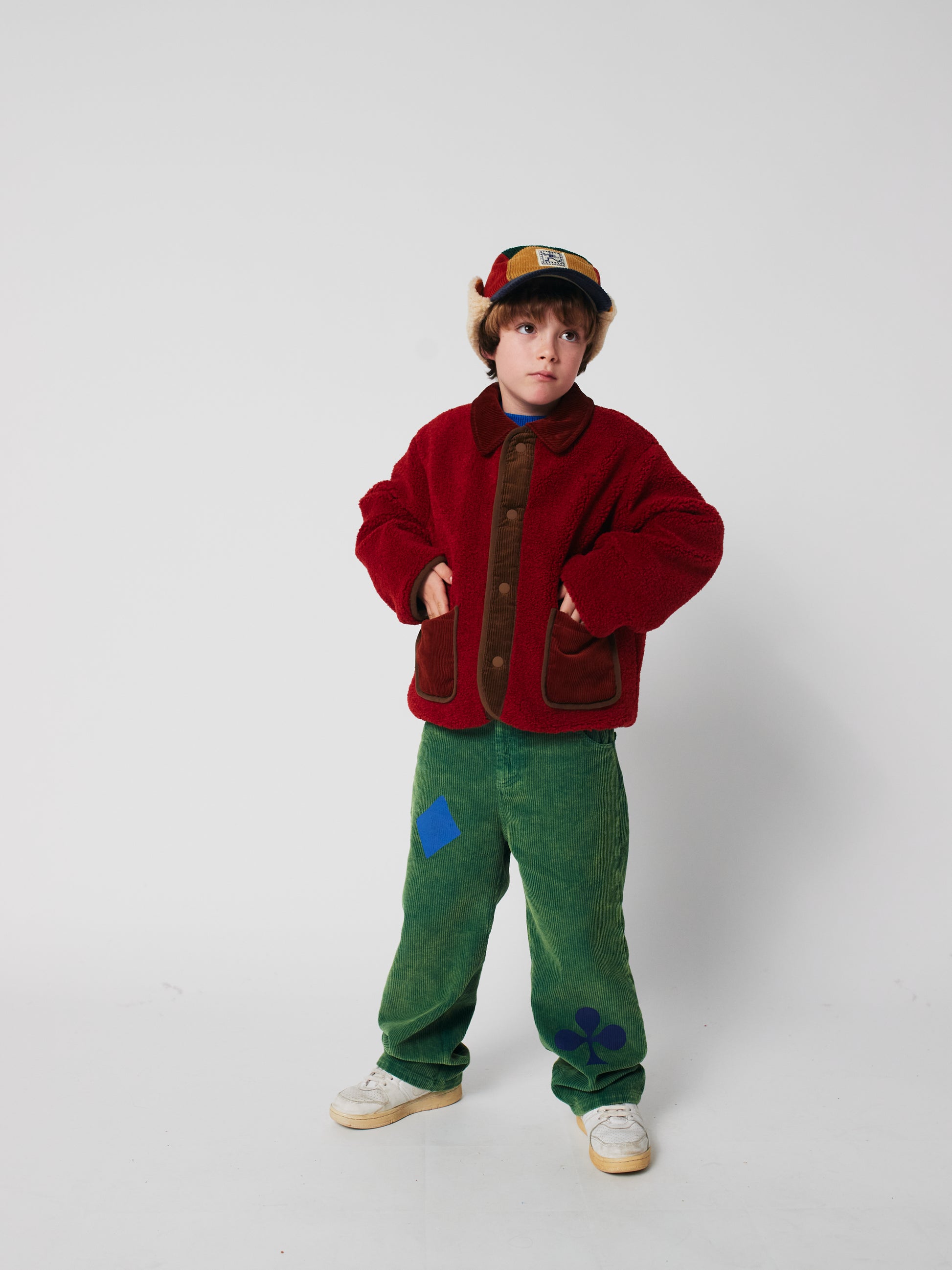 Child wearing a red jacket and green pants on a white background