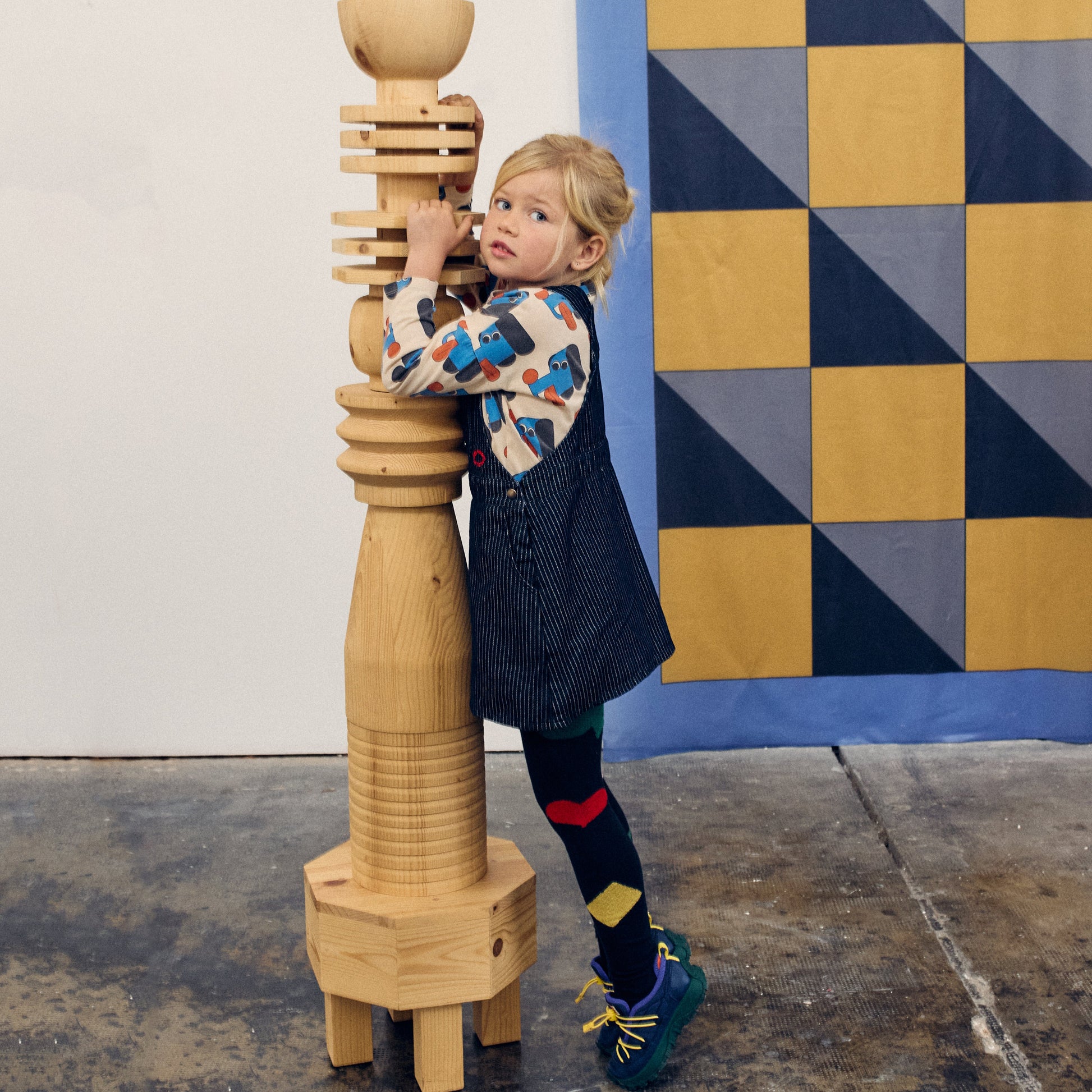 Child playing with a wooden sculpture against a geometric-patterned wall.