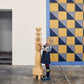 Child holding a wooden sculpture in front of a geometric patterned wall.