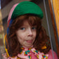 Person wearing a colorful outfit with a green hat and pink floral dress.