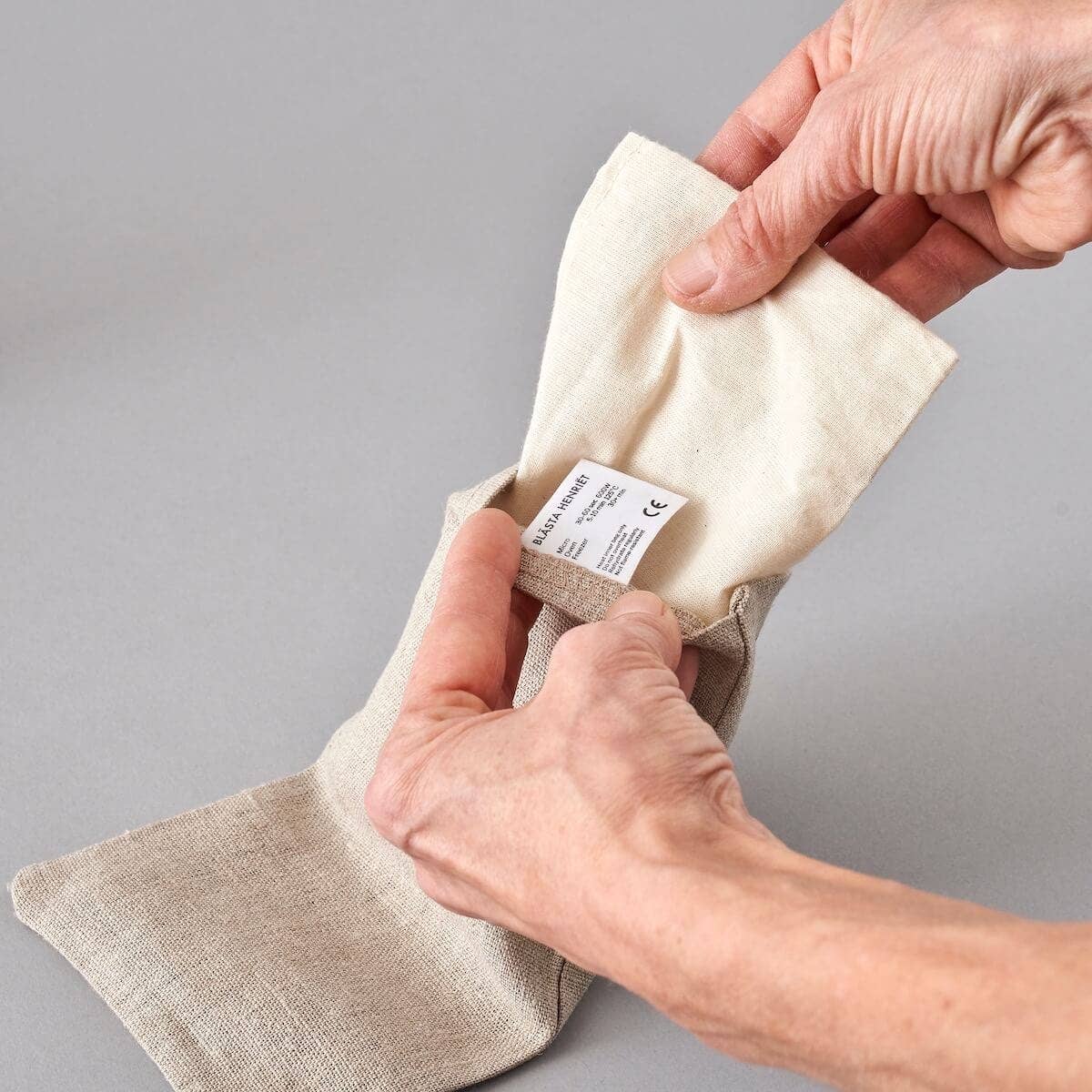 Close-up of hands removing the natural cotton inner bag from the linen cover of an eye pillow, showing its reusable and washable design.