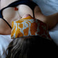 Person lying down with a yellow and white abstract-patterned linen eye pillow resting over their eyes for relaxation and comfort.