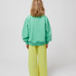 Bobo Choses A Day At The Beach Sweatshirt - Back View: A rear view of the child wearing the sweatshirt, showing the plain green back and gathered cuffs at the sleeves and hem.