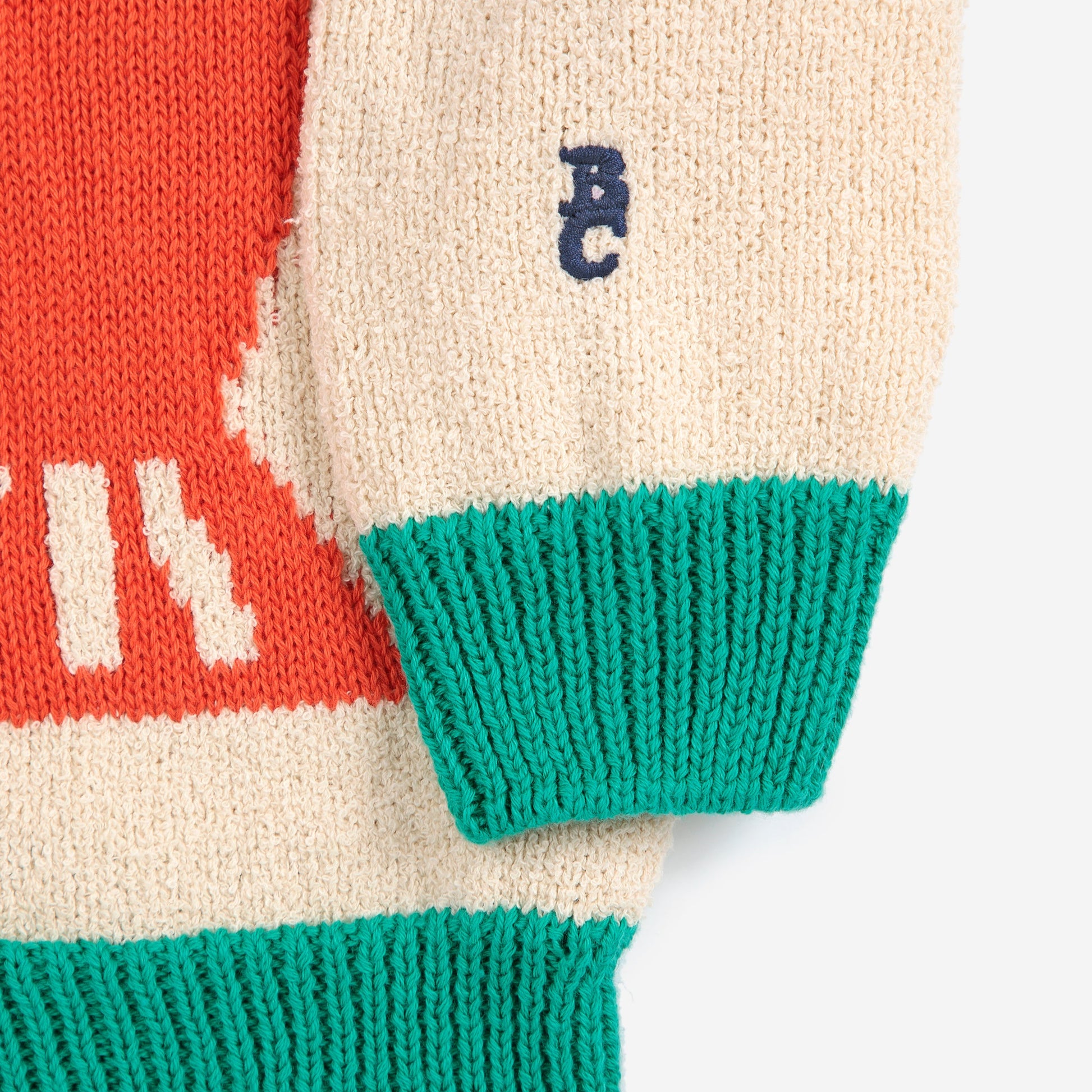 A detailed view of the cream-coloured sleeve with a navy blue embroidered "BC" logo near the wrist. The sleeve ends in a ribbed green cuff.