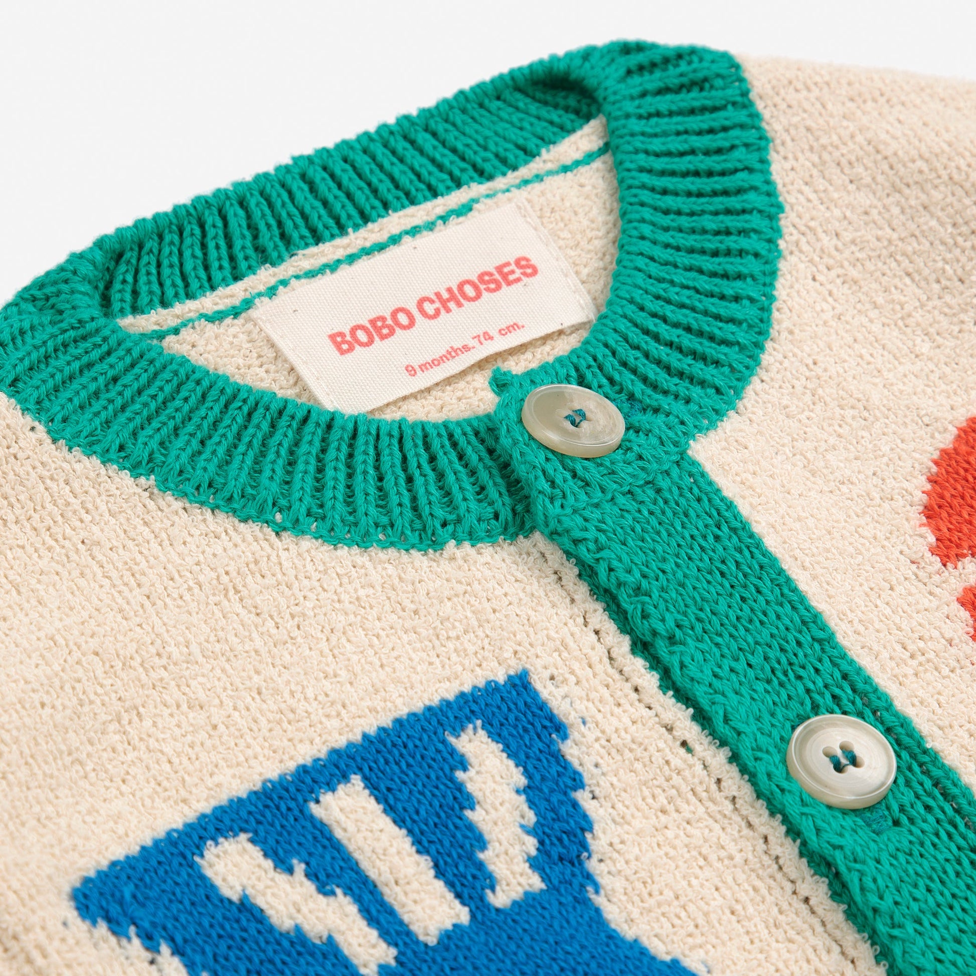 A detailed look at the green ribbed collar, cream button placket, and the Bobo Choses label stitched inside, showing the cardigan’s soft knit texture.