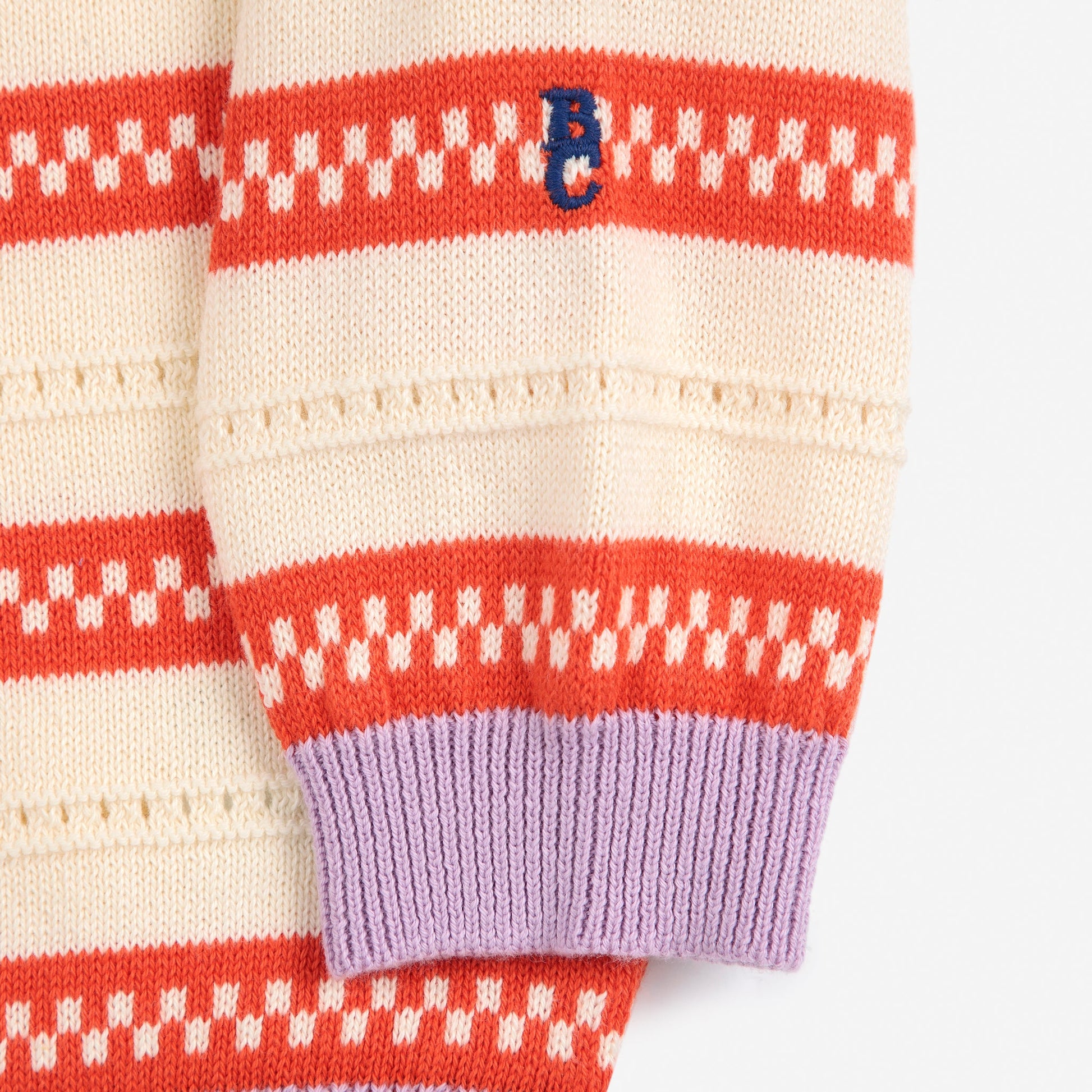 A look at the cream and orange striped sleeve with a small navy blue “BC” logo embroidered near the wrist. The sleeve ends in a lilac ribbed cuff.