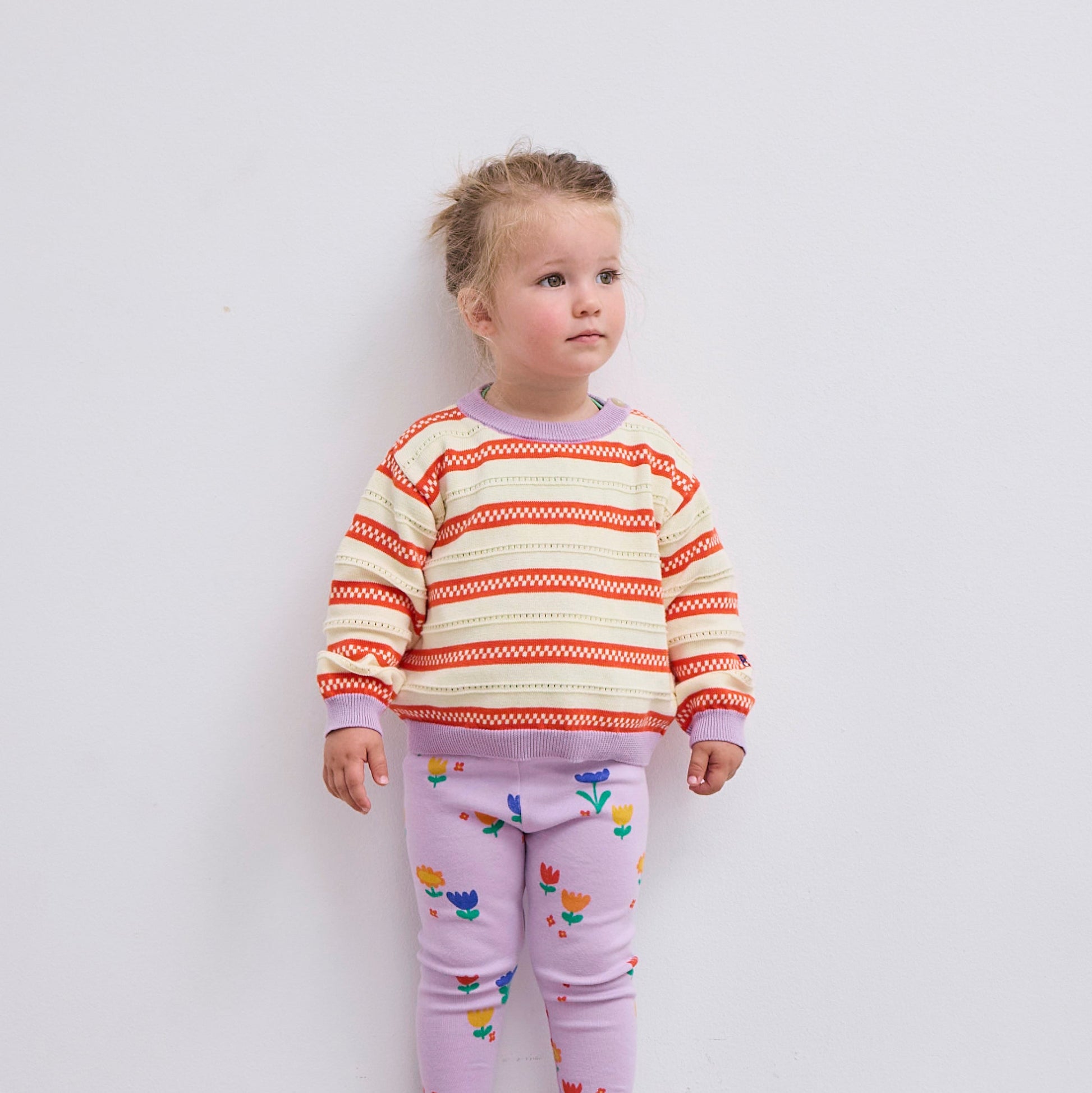 The child stands against a plain white background, showing the jumper’s relaxed fit and soft knit fabric.