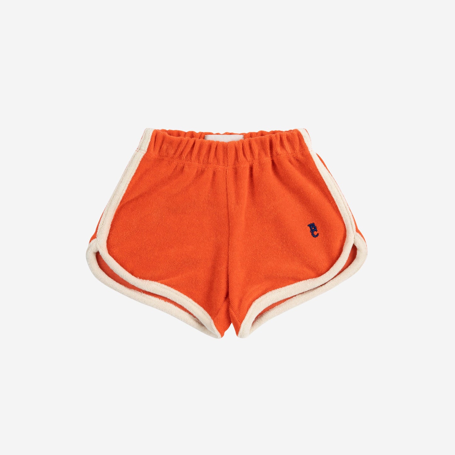 A pair of Bobo Choses baby terry cloth shorts in vibrant orange. The shorts feature an elasticated waistband and contrast cream piping along the curved hem. A small embroidered "BC" logo in navy is stitched on the lower left leg.