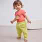 A toddler with short, wavy brown hair wears the gingham baby pants along with a coral pink T-shirt featuring a smiling face graphic and the "BOBO CHOSES" logo. The child is standing barefoot on a neutral floor.