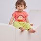 The same toddler sits on a white, modern-shaped cushioned seat while wearing the yellow gingham pants and coral T-shirt. Their legs are stretched out and slightly bent.
