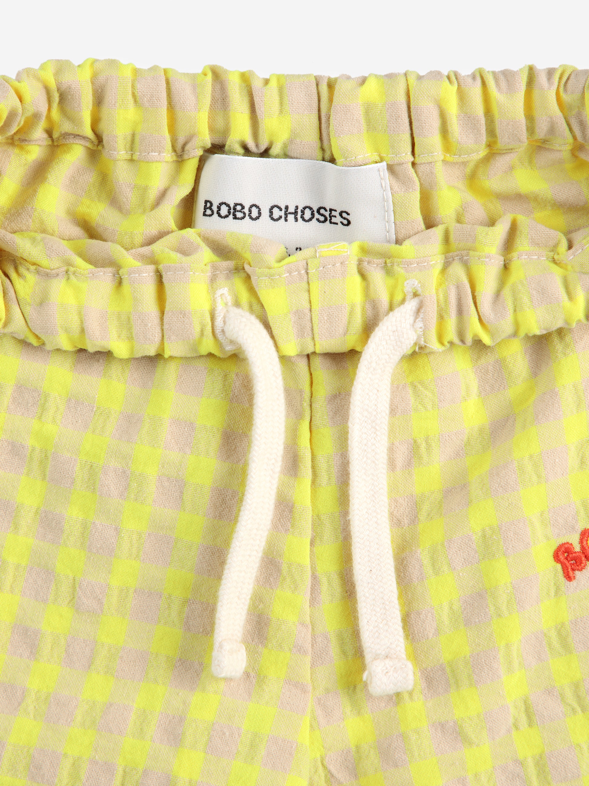 A close-up of the waistband of the baby pants, showing a cream drawstring and the "BOBO CHOSES" brand label sewn inside.