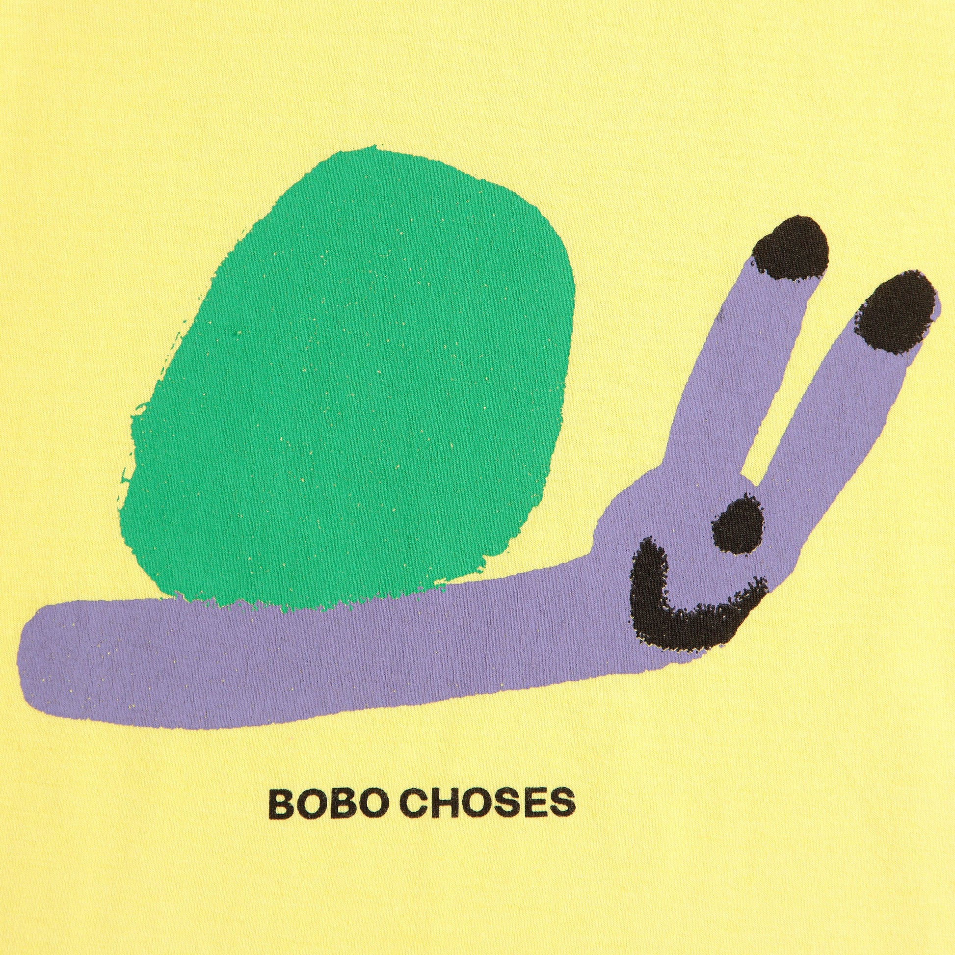 Close-up of the Bobo Choses Funny Snail T-Shirt design, featuring a playful illustration of a smiling snail. The snail has a bright green shell and a lavender body with black details on its antennae and face. Below the illustration, the text "BOBO CHOSES" is printed in black on the yellow fabric.