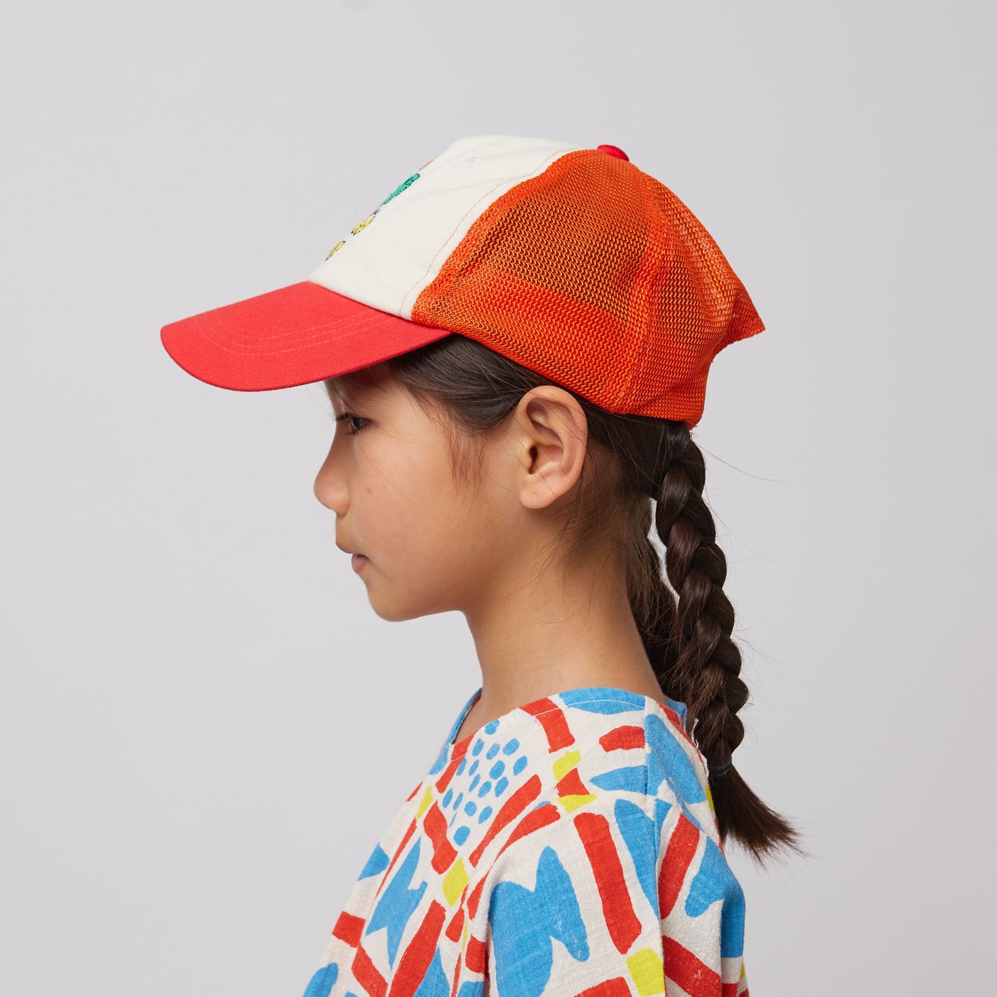 A profile view of the child wearing the Bobo Choses "Hello Joy" mesh cap, highlighting the bright orange mesh back and the adjustable strap.