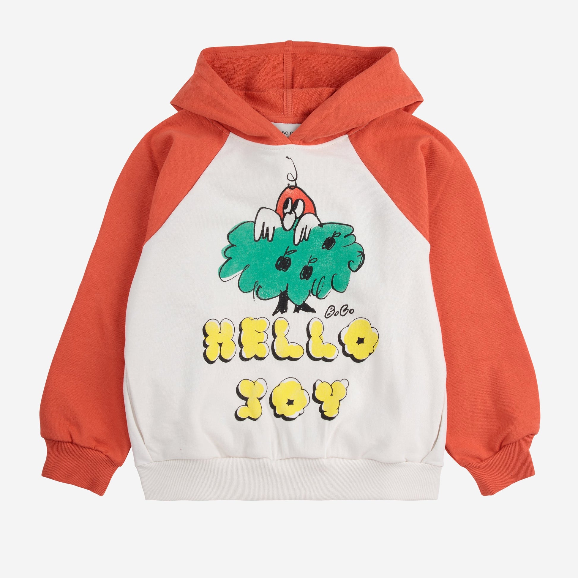 A children's hoodie with a white body and contrasting raglan sleeves in burnt orange. The front features a playful graphic of a small red character peeking out from a green bush, with "HELLO JOY" written in bold yellow bubble letters.
