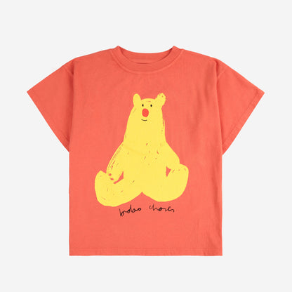 A short-sleeved children's T-shirt in a warm coral shade, featuring a large graphic of a yellow bear with a red nose sitting cross-legged. Below the bear, "Bobo Choses" is printed in a handwritten-style font.