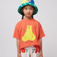 A young child with two braids is wearing the coral T-shirt with the yellow bear print. The child is also wearing a colourful bucket hat with blue, green, and yellow panels.