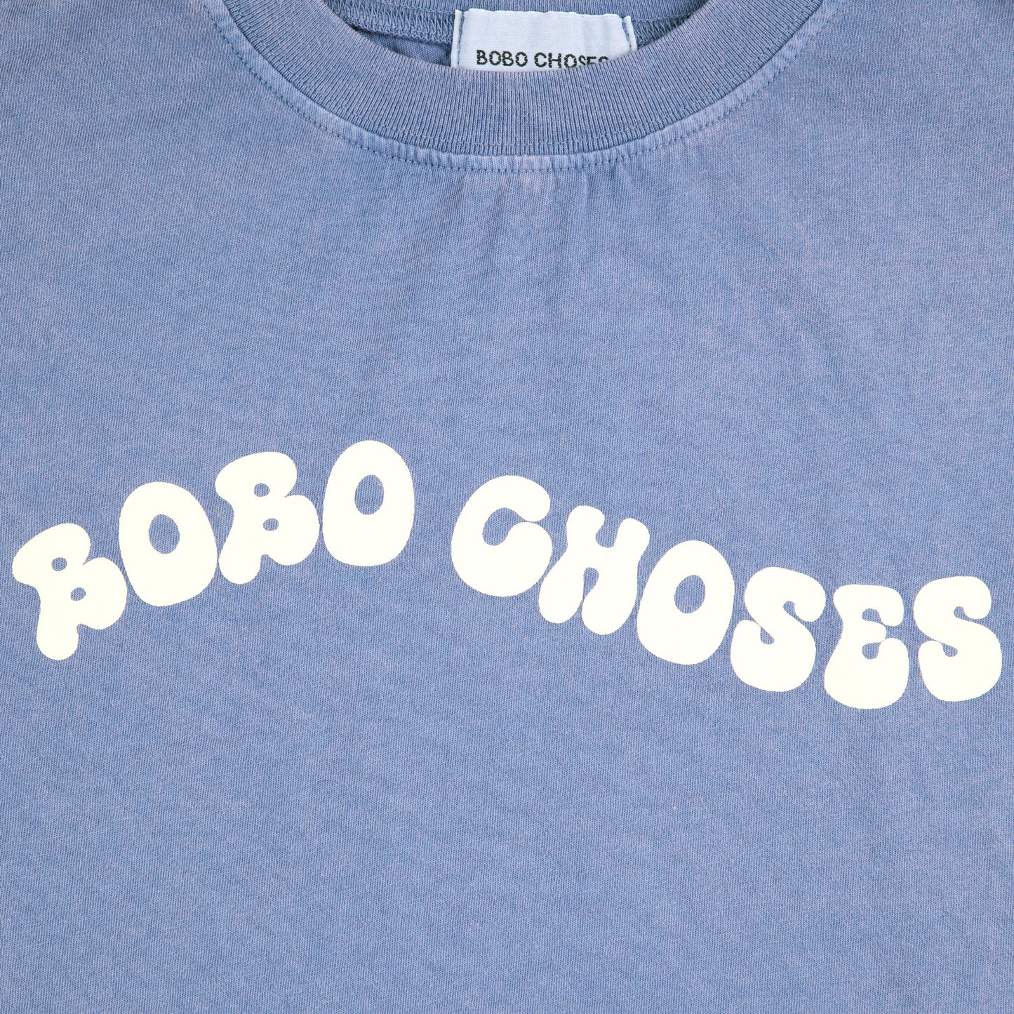 Close-up of the "BOBO CHOSES" wavy print in cream on the blue t-shirt.