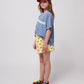 Side view of the girl wearing the blue wavy t-shirt with yellow sunflower shorts.