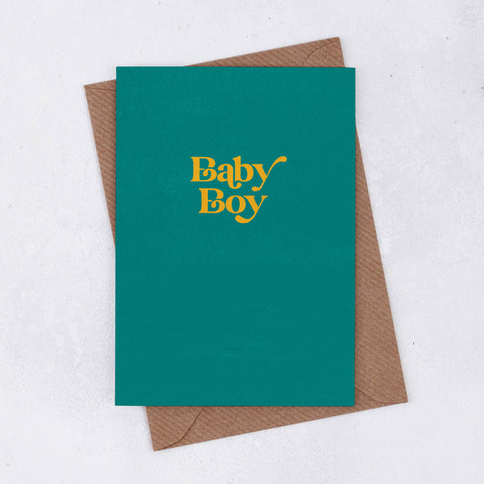 A brown Kraft envelope with a simple teal greeting card with the words Baby Boy on the front in a retro font