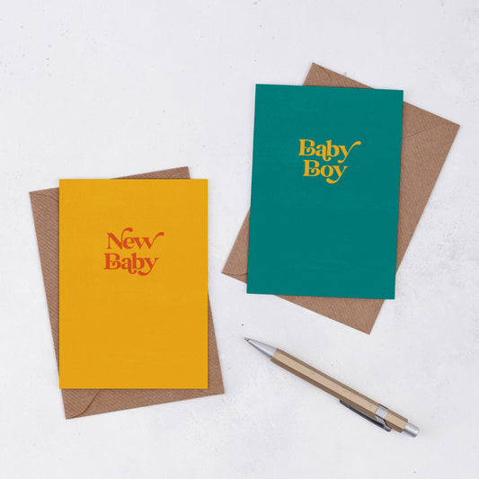 Two simple greeting cards with Kraft envelopes. One is bright yellow and says New Baby in red, and the other is teal with Baby Boy in yellow. The font is retro in style