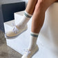 Person wearing white sneakers and socks with black stripes, sitting on a concrete block.