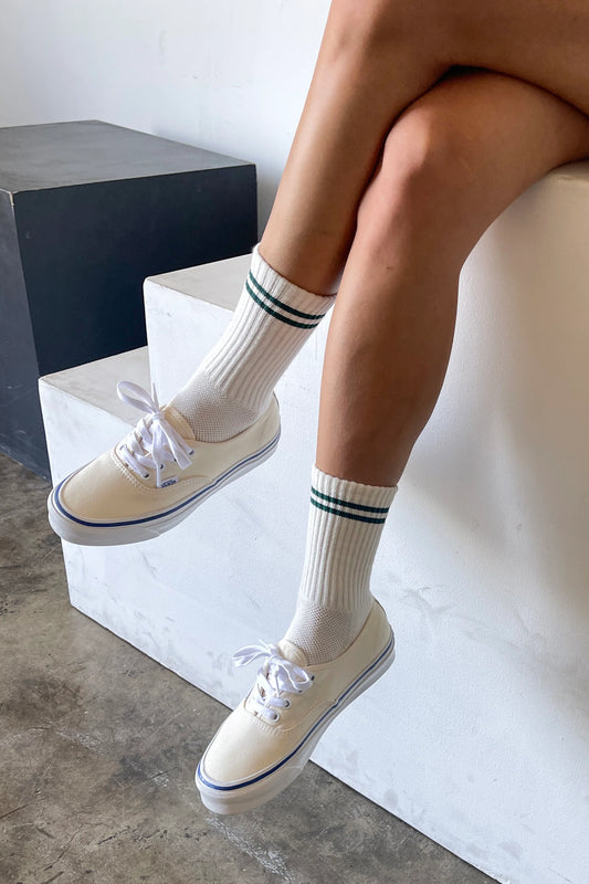Person wearing white sneakers and socks with black stripes, sitting on a concrete block.