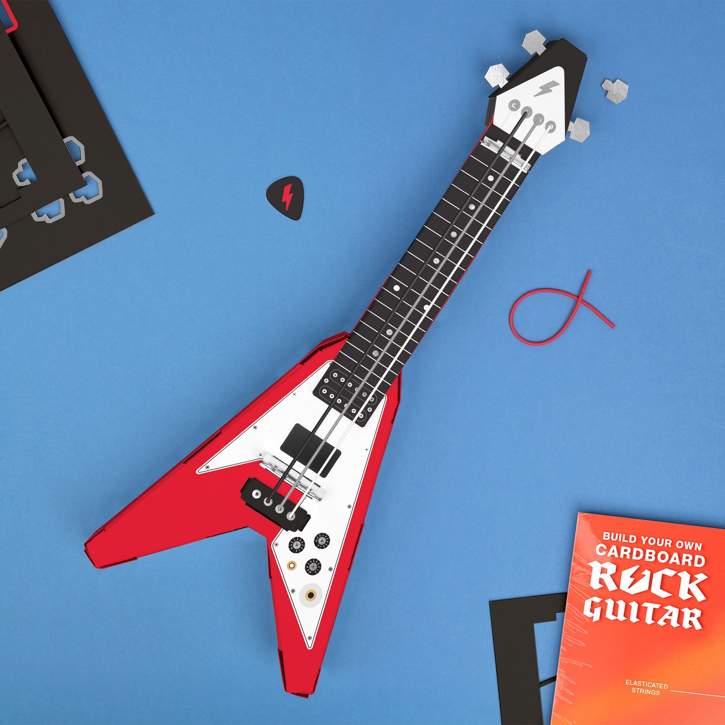 Red Build Your Own Rock Star Guitar – a playable cardboard Flying-V guitar kit featuring pop-out components that assemble without glue or tape. Elastic bands serve as strings, making it a fun DIY project for kids to create their own unique musical instrument. Perfect for imaginative play and creativity. Sits on a blue background with a guitar pick