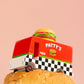 Toy truck labeled 'Patty's' on a large hamburger with a pink background