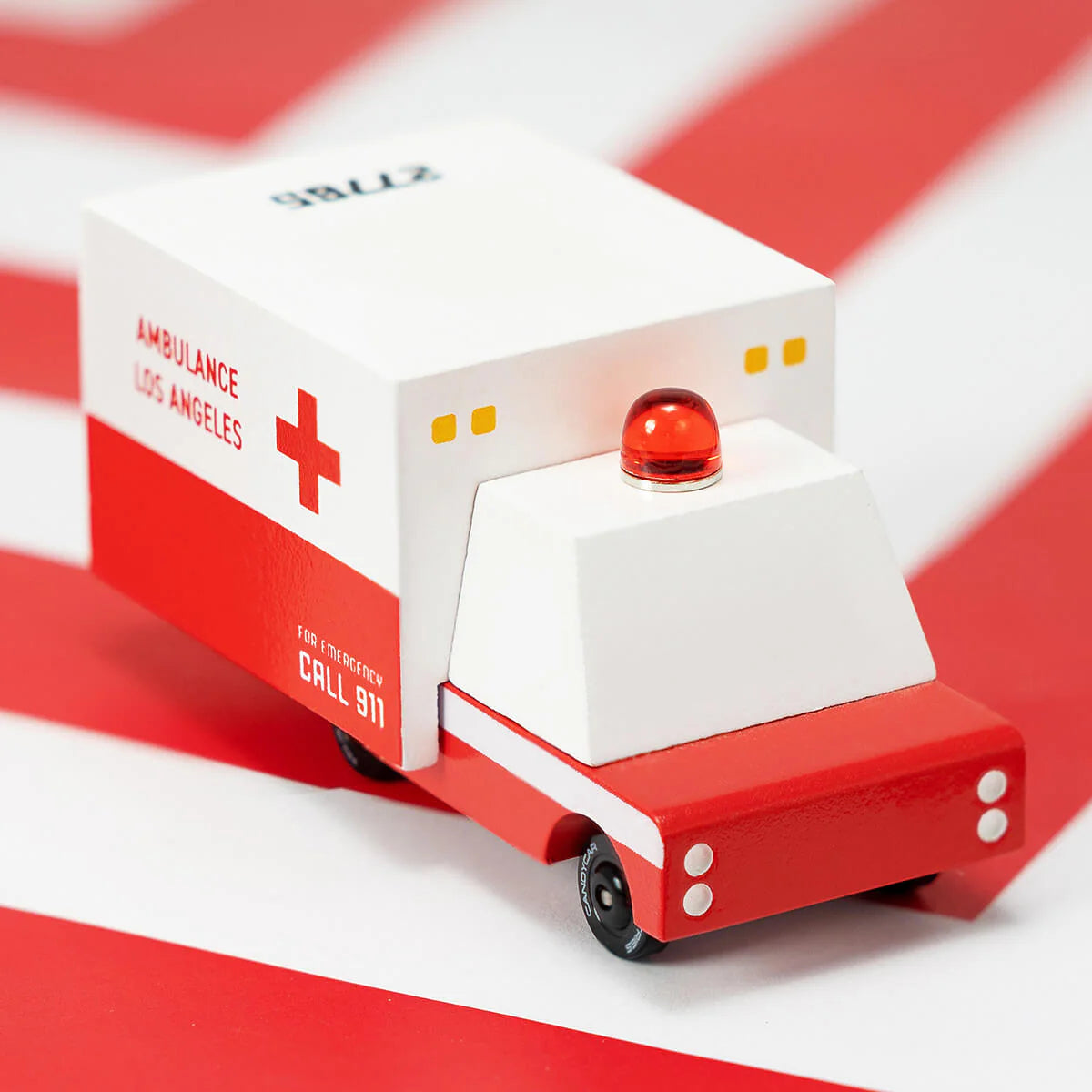 Model of a red and white ambulance toy on a red and white striped background