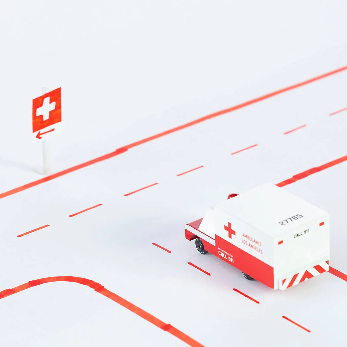 Model ambulance on a road with a medical cross sign in the background