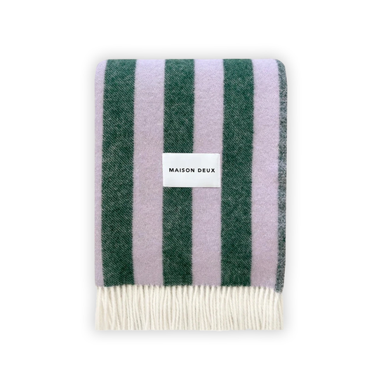 A striped blanket with alternating green and purple stripes, featuring fringes on the short sides and the Maison Deux brand tag visible.