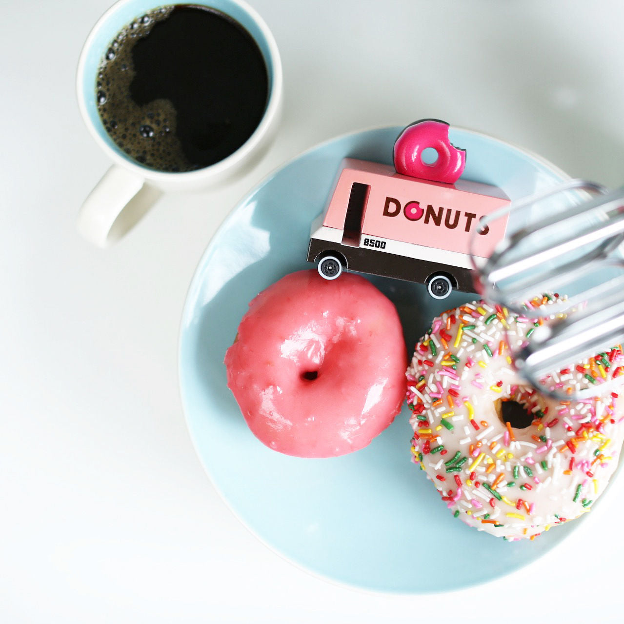 Two donuts on a plate with a coffee cup and a 'Donuts' truck toy.