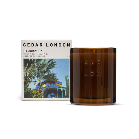 Cedar London Majorelle Candle in a refillable amber glass jar, embossed with 'CDR LDN,' next to its packaging featuring the iconic Majorelle Garden in Marrakech. Scent notes include neroli, sandalwood, oud, jasmine, and amber.