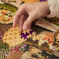 Hand placing a puzzle piece on a colorful puzzle with a scenic design.