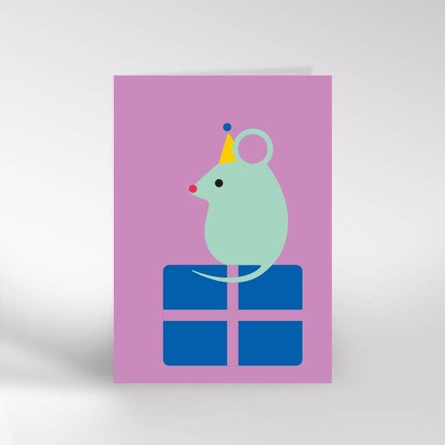 An A6 greeting card with the image of a blue mouse with a yellow party hat on sitting on top of a blue gift box. 