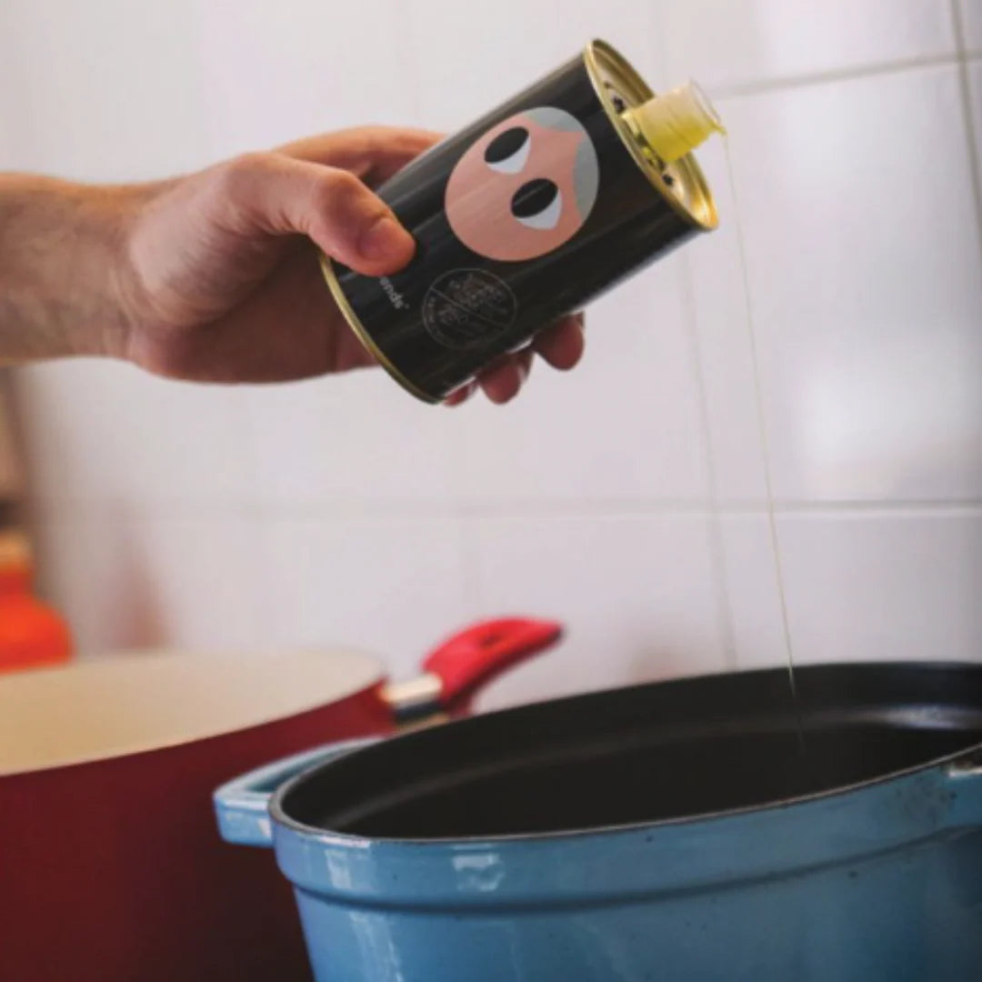 Person pouring oil from a can into a blue pot in a kitchen.